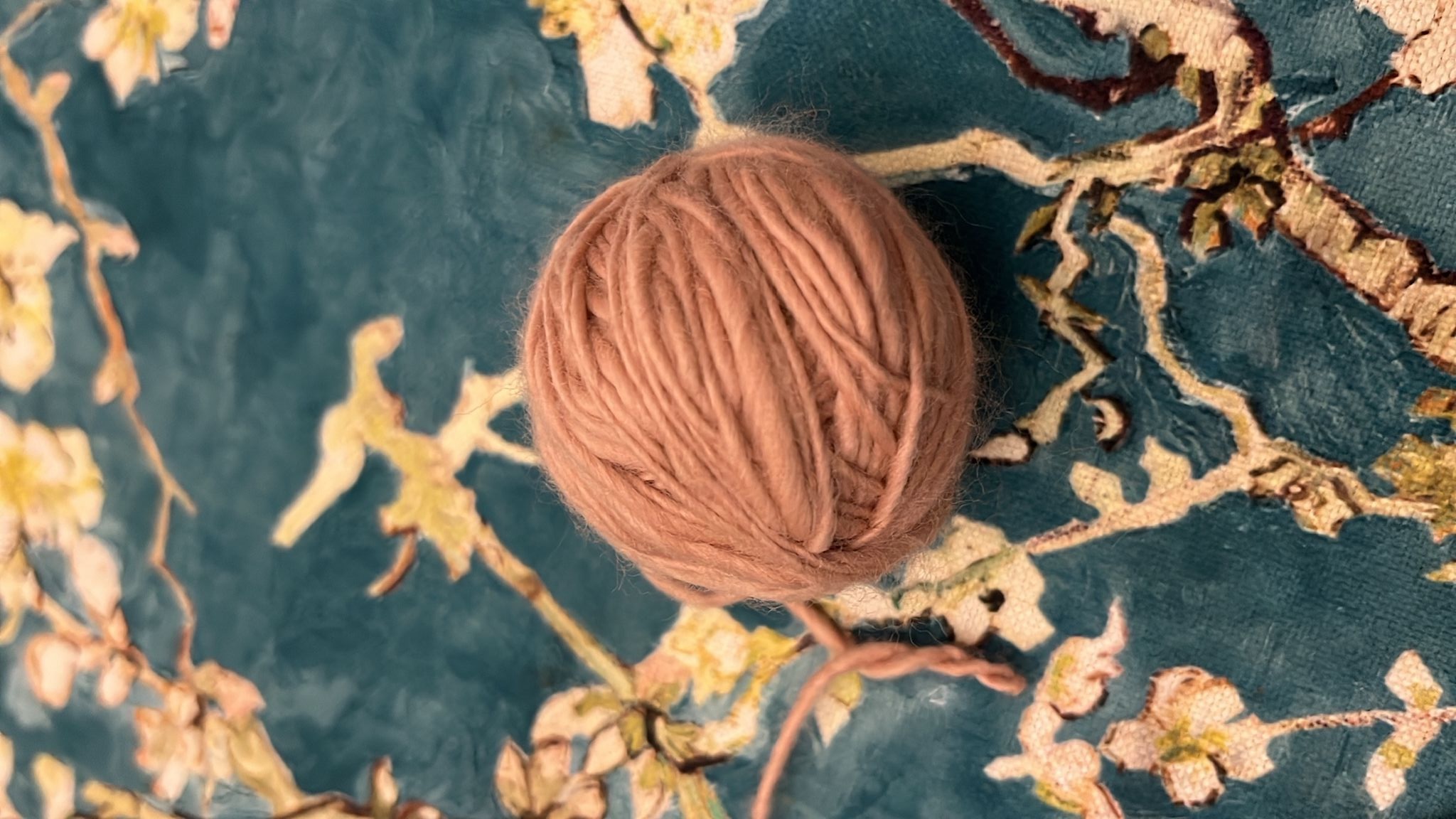 A ball of plant-dyed wool resting on cloth painted with almond blossom — natuRa.Ely slow-fashion atelier on Lake Garda