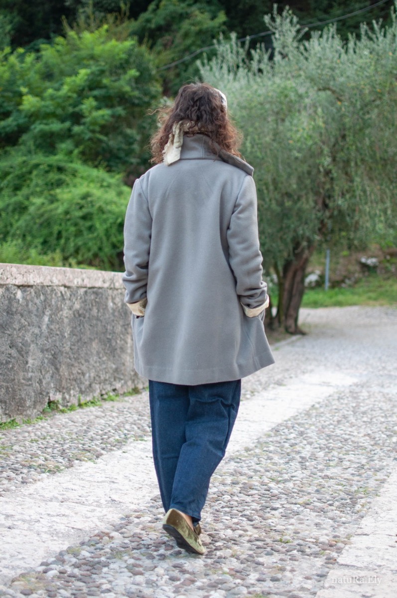 From behind, in Arco — Pelèr N° I, grey wool, cashmere and alpaca coat with standing collar, handmade in the natuRa.Ely atelier in Arco, Lake Garda