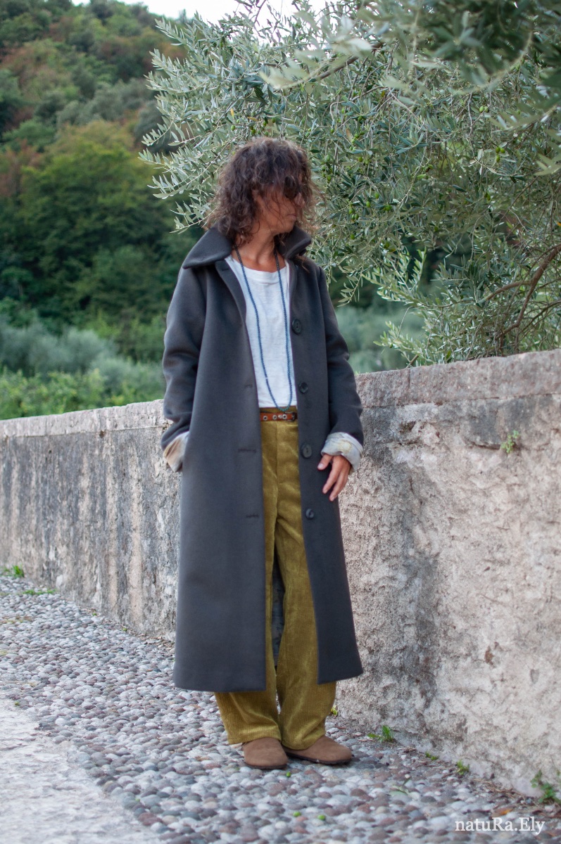 Front, beneath the olive tree — Pelèr N° IV, dark taupe wool and cashmere coat with concealed pocket, handmade in the natuRa.Ely atelier in Arco, Lake Garda