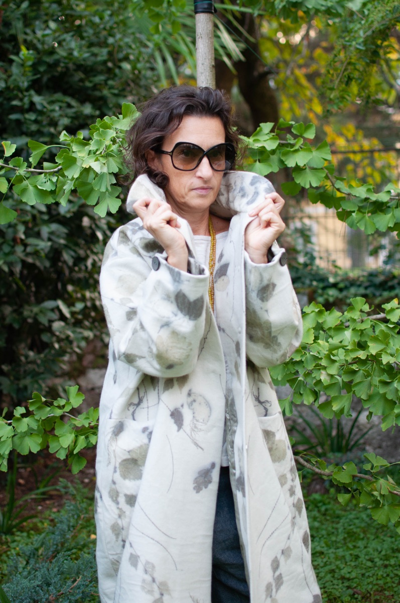 Pelèr N° V — coat in ecoprinted merino wool, standing collar held up by hand, under the ginkgo